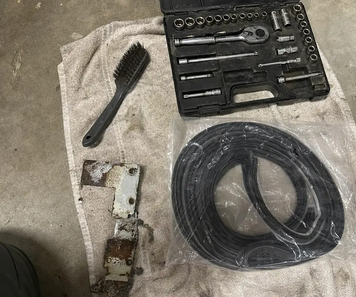 A corroded bracket removed from an appliance, lying on a towel beside a bagged replacement part