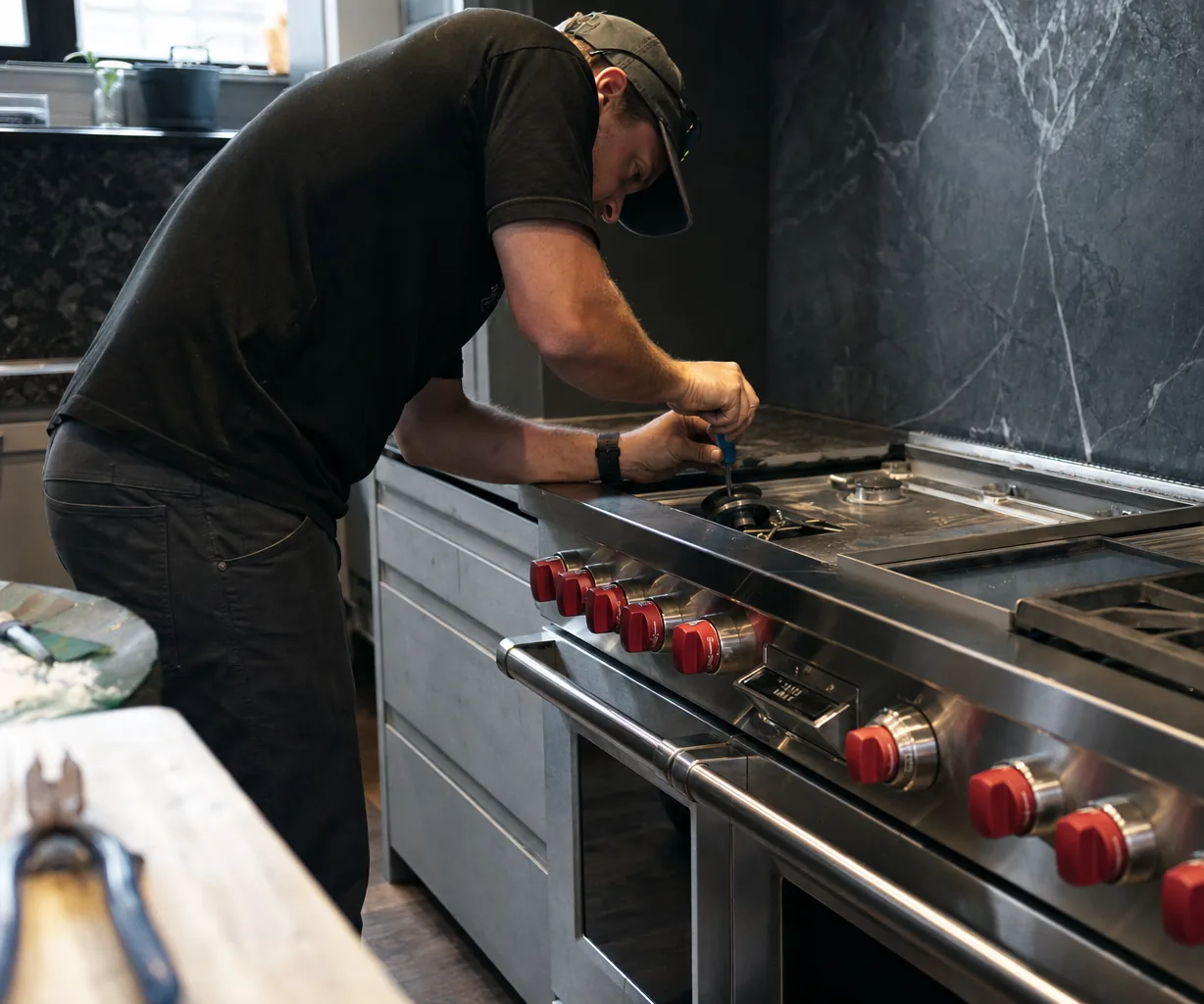 A stainless range and the run of cabinetry beside it in a large kitchen, a grate set aside on the counter